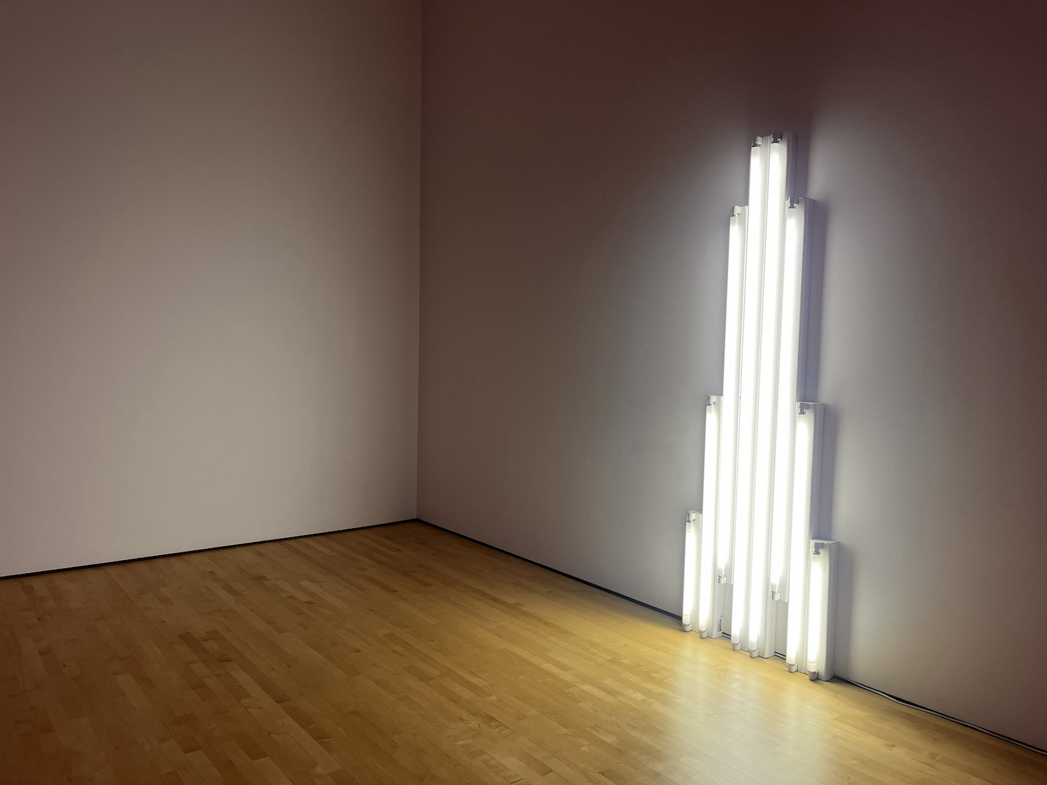 Disability Accessibility at SFMOMA. "Monument" for V. Tatlin by Dan Flavin. A white fluorescent neon light sculpture, reminiscent of a memorial shaped tower or pillar. It sits opposite of another Dan Flavin piece, with these two pieces being the only artworks that activate the space with neon light.