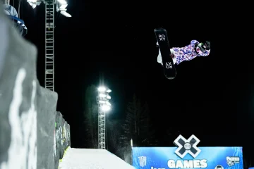 Female Snowboarder Jumping out of the halfpipe with X Games logo in background | Photo by X-Games Website